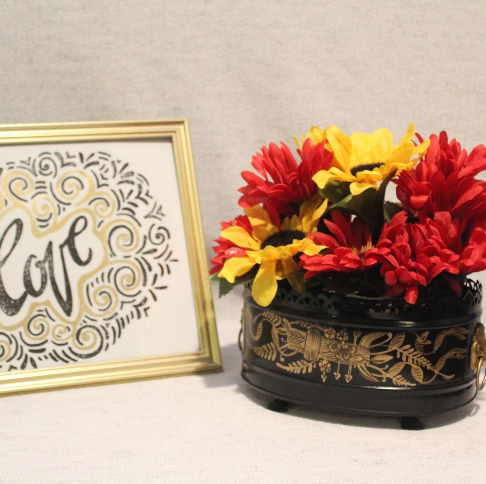Artificial flowers in a black and gold base.